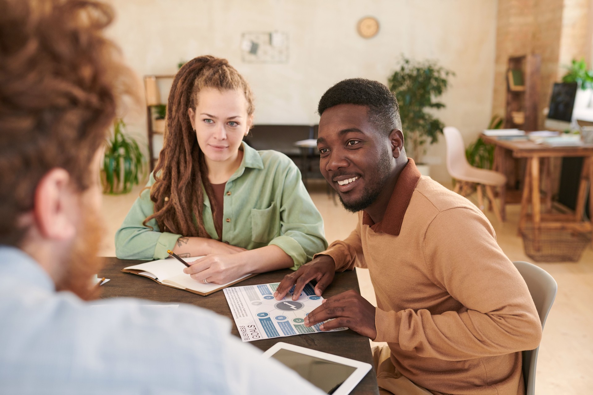 Smiling young African-American marketer listening to colleagues idea while they collaborating in modern office