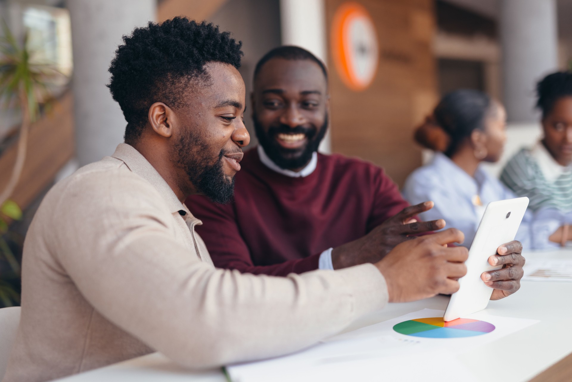 Two african american businessmen using tablet and analyzing financial charts in modern office